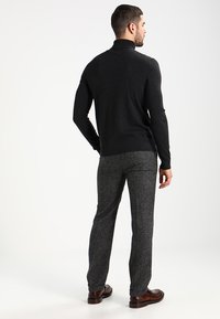 Donkergrijze turtleneck sweater met lange mouwen, gecombineerd met lichtgrijze gestructureerde broeken en bruine schoenen. Eenvoudig, strak ontwerp.