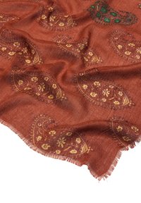 Szalik w kolorze rdzy z wzorem paisley w żółtym i zielonym kolorze. Miękka tekstura i frędzlowane krawędzie, ukazujące misternie wykonane detale kwiatowe.