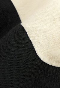 Zwarte en crèmekleurige stofmix met een gladde textuur, voorzien van een gebogen kleurblokontwerp. Zichtbare stiksels langs de randen voegen detail toe.