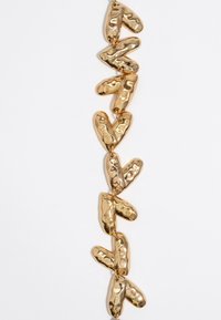 Pulsera de cadena en tono dorado que presenta eslabones en forma de corazón pulidos con una textura martillada. Los eslabones están conectados por anillos de metal simples.