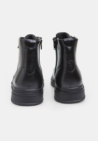 Botas de tobillo de cuero negro con un acabado suave, que cuentan con una suela de goma texturizada y cierre lateral con cremallera. Construcción resistente, detalles mínimos.