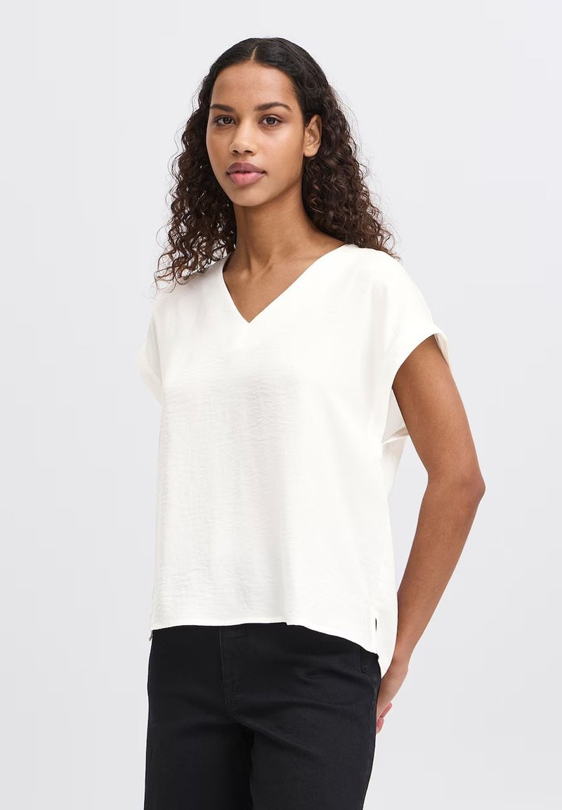 Top bianco a maniche corte con scollo a V e vestibilità rilassata, caratterizzato da un tessuto leggermente strutturato e un'orlo arrotondato con sfiocchi laterali.