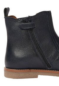 Bottine en cuir bleu marine foncé avec une finition texturée, fermeture éclair latérale et une semelle en caoutchouc tan basse. Elle dispose d'une petite boucle à l'arrière pour un enfilage facile.