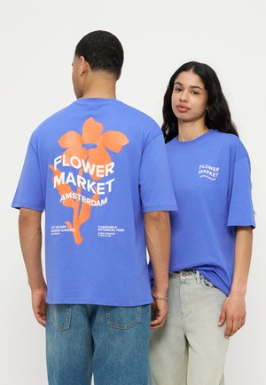 To personer iført blå T-shirts med teksten "Flower Market Amsterdam"; den ene vender fremad, den anden vender bagud og viser en stor orange blomst.
