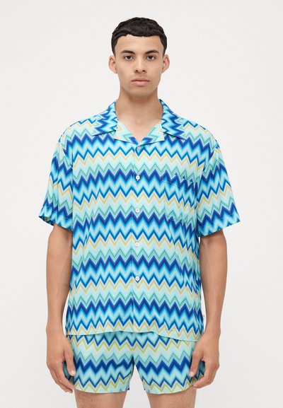 Korte mouwen overhemd met knopen en shorts in een blauw en groen zigzagpatroon. Gemaakt van een gladde, lichte stof.