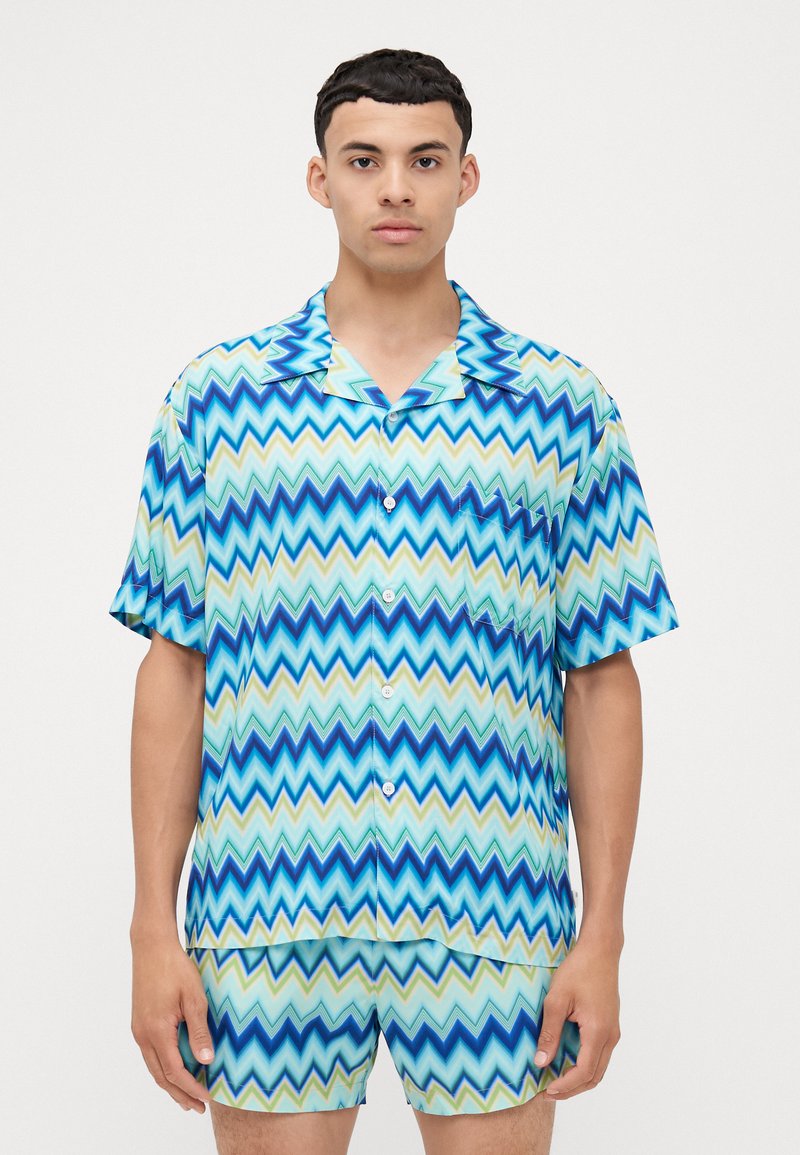 Set di camicia a maniche corte con bottoni e pantaloni corti in un motivo zigzag blu e verde. Realizzato in un tessuto leggero e morbido.