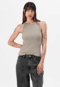 Ribbet beige tanktop med høy hals og ermeløs design, kombinert med høyhøyde mørk denim jeans med frontlommer.