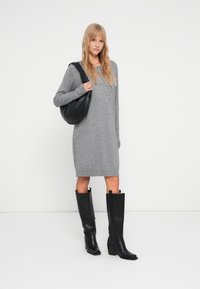 Robe en tricot gris avec un ourlet à côtes, associée à des bottes en cuir noir jusqu'au genou avec un talon bloc. Un sac à épaule noir est également inclus.