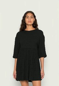 Vestido preto de manga curta com um design texturizado e plissado. Apresenta um corte relaxado e um decote redondo, caindo acima do joelho.