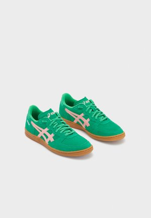 Green suede sneakers with pink accents, featuring a rounded toe, flat laces, and gum rubber sole for grip and comfort.