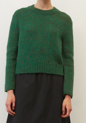 Loose-fitting green knit sweater with long sleeves paired with high-waisted black skirt, shown from neck to hips.