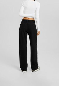 Vaqueros de mezclilla negra de pierna ancha con cintura alta, que cuentan con bolsillos traseros y una textura suave, combinados con un top blanco ajustado de manga larga.