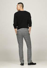 Schwarzer Strickpullover, graue karierte Hose mit taillierter Passform und schwarze Schuhe. Das Outfit hat eine strukturierte Optik und dezente Akzente.