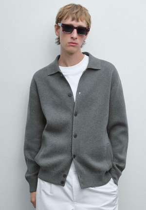 Gray knitted cardigan with a collared neck, five dark buttons, and a textured finish, worn over a white shirt.