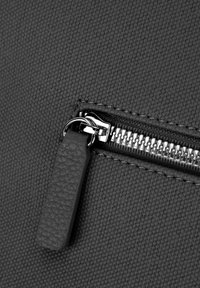 Schwarze Stofftasche mit einem Reißverschluss und einem glänzenden metallischen Zipper, strukturiertem Ziehgriff und genähten Kanten, die Haltbarkeit und Funktionalität betonen.