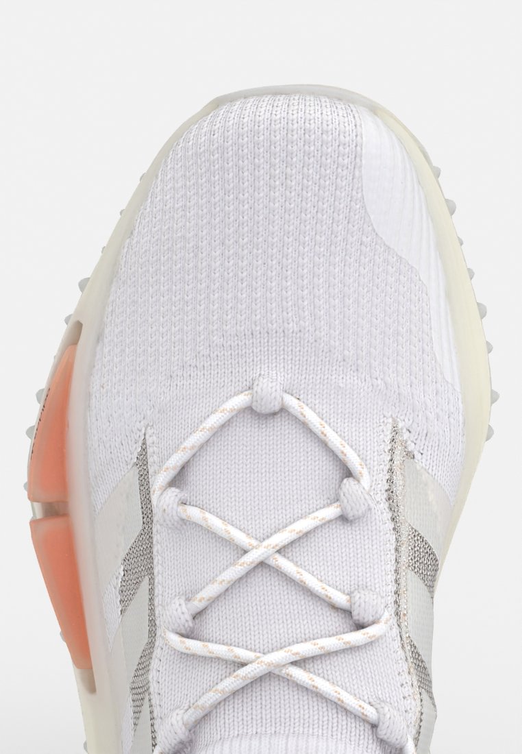 Zapatilla textil blanca con parte superior de punto, acentos reflectantes y suela de goma con un talón y sistema de cordones de color naranja claro.