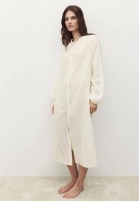 Robe chemise blanche longue à boutons, à manches longues, fabriquée en tissu léger, avec une coupe droite et un subtil éclat.