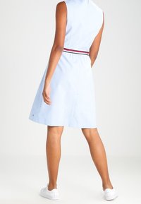 Hellblaues ärmelloses Kleid mit taillierten Schnitt, ausgestellt Rock und rot-blau gestreiftem Akzent an der Taille. Getragen mit weißen Sneakers.