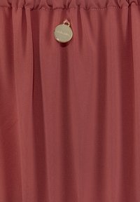 Tissu bordeaux froncé avec une texture lisse, doté d'une étiquette circulaire dorée avec le nom de la marque. Convient à divers designs de vêtements.