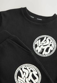 Črn pulover z okroglim belim logotipom z bolj stiliziranim napisom. Iz mehkega materiala, z okroglim izrezom in rebrastimi manšetami.