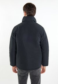 Schwarze gepolsterte Jacke mit hohem Kragen, featuring eine glatte Außenseite und gesteppte Details, kombiniert mit grauen schmal geschnittenen Jeans.