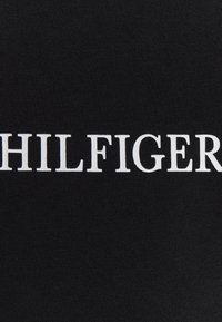 Czarna tkanina z dużymi, wyraźnymi białymi literami tworzącymi napis "HILFIGER". Tekstura wydaje się gładka i lekko elastyczna.