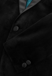 Blazer de terciopelo negro con delantero y puños de manga abotonados, mostrando parcialmente el forro interior de satén en color verde azulado.