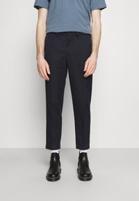 Pantalons bleu marine en coton, avec une coupe droite, une taille mi-haute et des poches avant. Associés à des bottines noires et des chaussettes blanches.