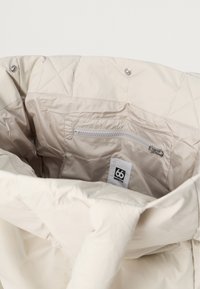 Lichtbeige geïsoleerde jas met een gevoerde textuur aan de binnenkant, voorzien van een ritszak en een merklabel met de tekst "66° North."