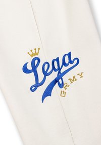 Biały materiał zdobiony niebieskim i złotym haftem. Napis "Lega" w kursywie z "GRMY" poniżej, podkreślony małą koroną powyżej.