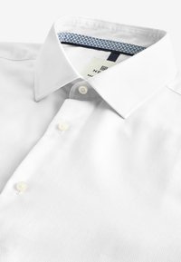 Weißes Baumwollhemd mit strukturiertem Gewebe, Button-Down-Kragen und Perlmuttknöpfen. Der innere Kragen hat ein blaues geometrisches Muster.