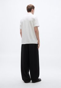 Fehér rövid ujjú galléros póló egyszerű gallérral és kontrasztos szegéllyel, laza fekete nadrággal és lapos talpú cipővel párosítva.