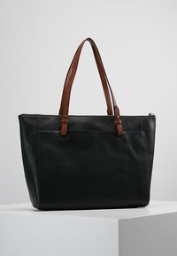 Zwarte leren tote tas met twee bruine schouderbanden, een ritssluiting en een voorvak. Gladde textuur, gestructureerde vorm, minimalistisch ontwerp.
