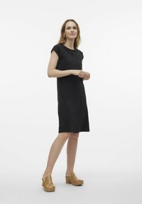 Robe noire à manches courtes avec une coupe ample, dotée d'un col rond et d'une texture lisse. Associée à des sabots en bois à talons épais couleur tan.