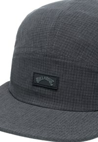 Grey bucket hat made of textured fabric with a checkered pattern. Features a rectangular black patch with white lettering.