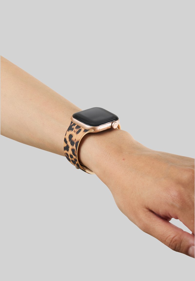 Smartwatch z ramką w różowym złocie i czarnym ekranem na nadgarstku, z paskiem w panterkę na jednolitym szarym tle.