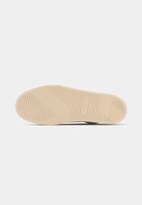 Beige kummist sneakerite tald horisontaalsete soonte ja tekstuuriga haardumiseks. Ümar kuju, mille pind on sile ja ühtlane.