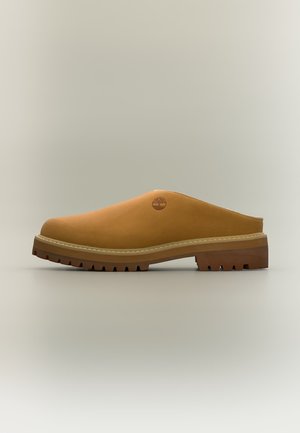 Ταμπά mule παπούτσι slip-on με χοντρή ανθεκτική σόλα και το λογότυπο δέντρου Timberland στο πλάι, εμφανίζεται σε απλό ανοιχτό φόντο.