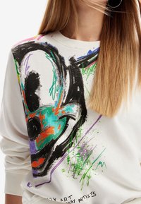 Felpa bianca con un grafico astratto colorato caratterizzato da linee audaci e spruzzi di arancione, verde e blu, progettata con una vestibilità rilassata.