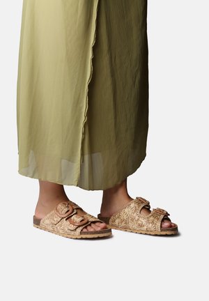 Klapki na płaskiej, gumowej podeszwie z teksturowanym, beżowym, plecionym wierzchem, wyposażone w dwie regulowane klamry. Podeszwa wewnętrzna ma naturalny kolor korka.