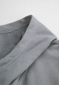 Szary sweter z miękką teksturą, z kapturem i prostym wzornictwem. Zbliżenie pokazuje splot i detale przeszycia materiału.