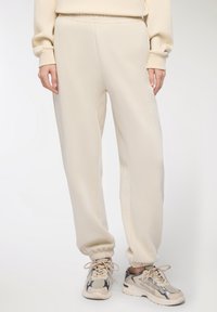 Pantaloni della tuta color crema con vita elastica e polsini, caratterizzati da una texture del tessuto liscia e cuciture laterali per una vestibilità comoda.