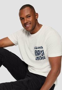 Witte katoenen t-shirt met een marineblauwe grafische zakontwerp. Draagt samen met zwarte cargobroeken, met een ontspannen pasvorm en een soepele textuur.