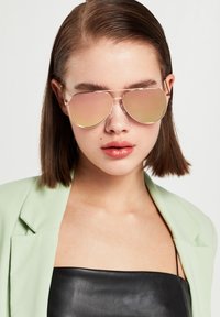 Sluneční brýle ve tvaru aviator v odstínu růžového zlata s zrcadlovými skly, disponující tenkým kovovým rámem a zdobené jemnými detaily hardware.