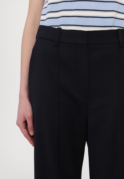 Maßgeschneiderte schwarze Hosen mit glatter Textur, mit flachem Vorderteil, seitlichen Taschen und Gürtelschlaufen, kombiniert mit einem blau-weißen gestreiften Oberteil.