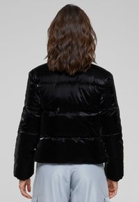 Svart boblejakke med en glanset, kviltet tekstur, med en kort design og ribbestrikkede mansjetter. Bakview som viser horisontale sømdetaljer.
