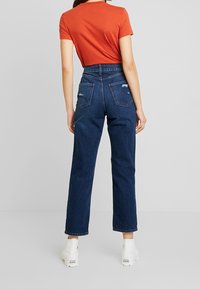 Höga, mörkblå denimjeans med avslappnad passform, två bakfickor och fransdetaljer. Kombinerade med en åtsittande orange T-shirt.