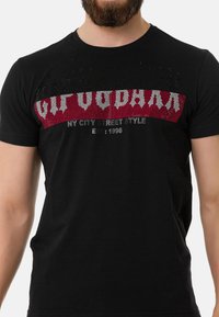 Zwarte katoenen t-shirt met een rood en zilveren grafisch ontwerp op de borst met de tekst "NY CITY STREET STYLE EST: 1996" in een vette lettertype.