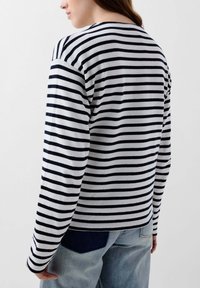 Long-sleeve striped top in white and navy. Features a round neck, relaxed fit, and soft texture. Visible seam details and casual styling.