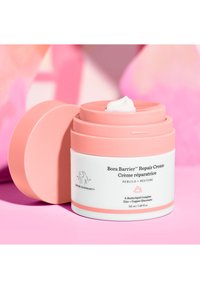 Pink cylindrical jar of Bora Barrier™ Repair Cream with a white label. Cream texture visible on the lid, featuring rounded edges and a contrasting white base.
